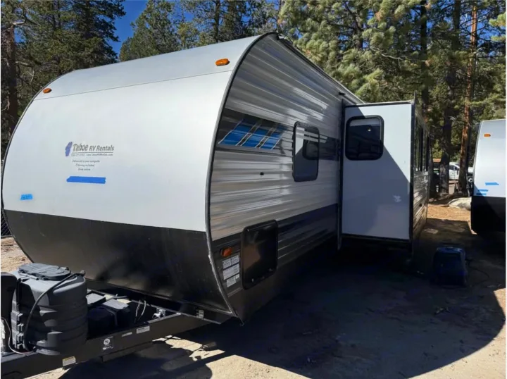 This rv rental, a white travel trailer from Tahoe RV Rentals, is parked outdoors with a slide-out extended among trees.. Forest River Salem 2022