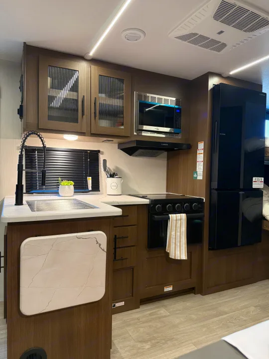 Enjoy a fully equipped RV rental kitchen with a modern sink, stove, microwave, and large refrigerator in this travel trailer.. Forest River Wildcat One 241DBEDS 2026
