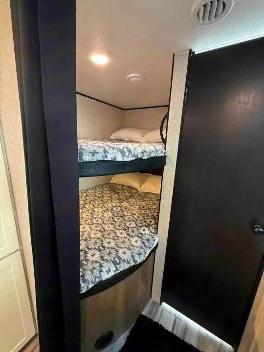 Cozy bunk beds in an RV rental, featuring patterned bedding, a black privacy curtain, and a ceiling light.. Jayco Jay Flight SLX 2025