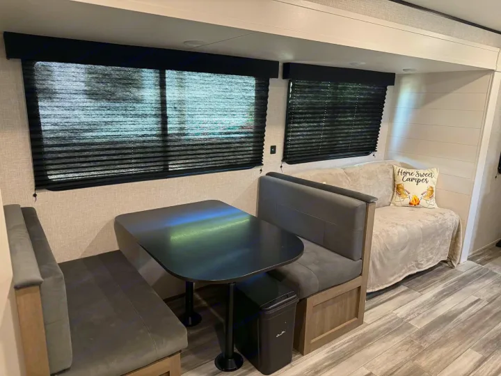 RV rental: Dinette booth, dark table, window blinds, and a sofa with a "Home Sweet Camper" pillow in a cozy interior.. Jayco Jay Flight SLX 2025