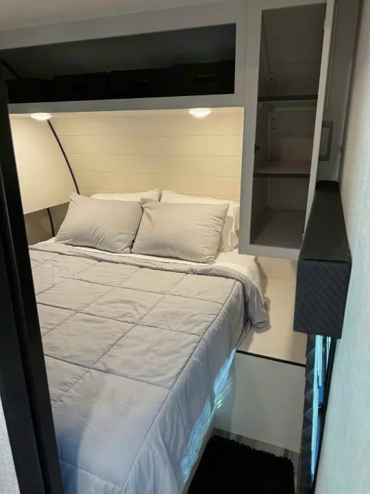 Cozy rv rental bedroom featuring a light gray bed with pillows, shiplap headboard, overhead lighting, and built-in cabinet storage.. Jayco Jay Flight SLX 2025