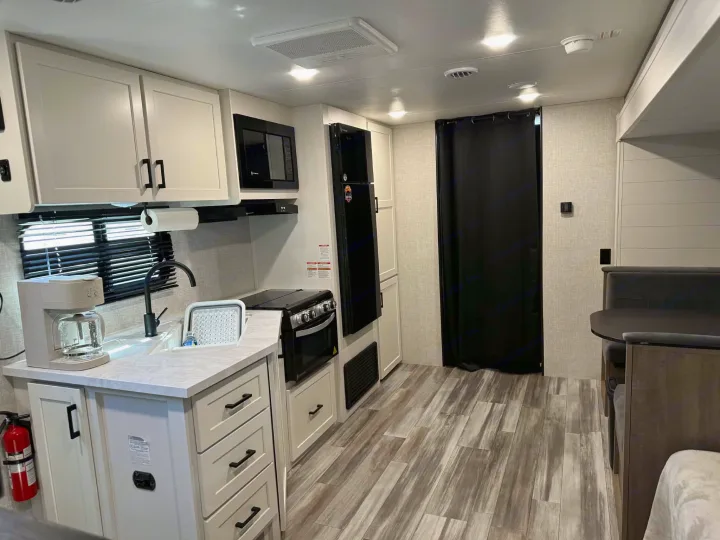 This rv rental features a modern kitchen with light cabinets, a dining area, and wood-look flooring, ideal for travel.. Jayco Jay Flight SLX 2025