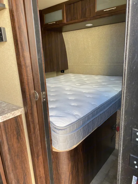RV rental bedroom interior: a plush white mattress sits on a bed platform, surrounded by dark wood cabinets and light paneled walls.. Forest River XLR HyperLite Toy Hauler 2017