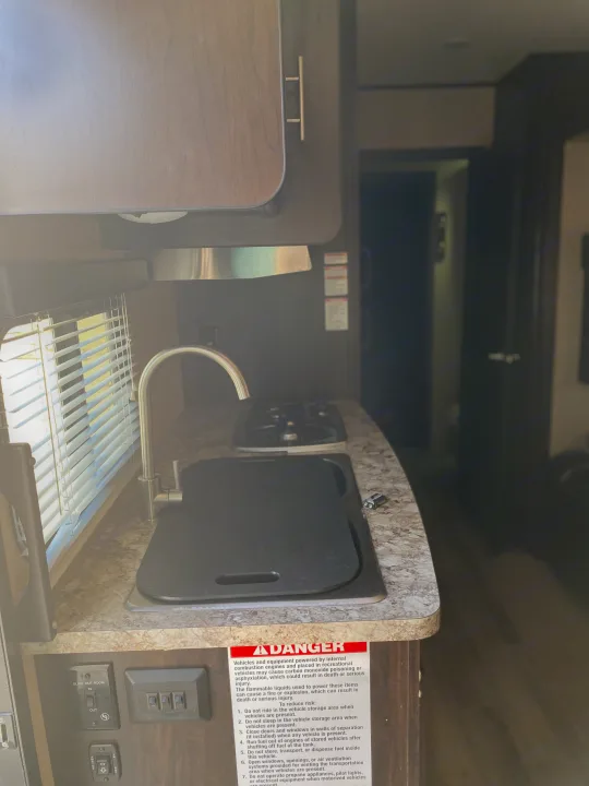 Inside an RV rental: a compact kitchen features a sink, stove, window, controls, and a safety warning. Ready for travel.. Forest River XLR HyperLite Toy Hauler 2017