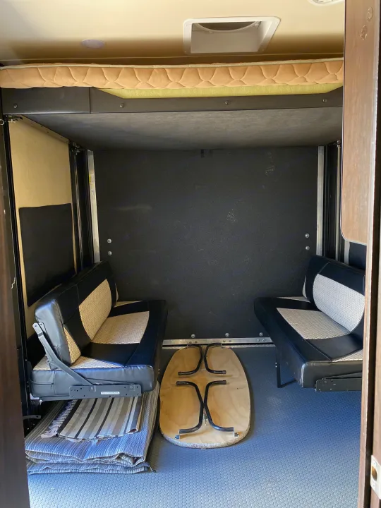 RV rental interior: versatile garage space with a fold-up bunk, side benches, and a stowed table on patterned flooring.. Forest River XLR HyperLite Toy Hauler 2017