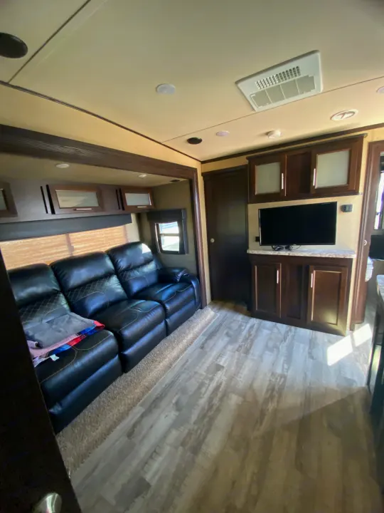 Spacious RV rental living area features black leather recliners, wood-look flooring, and ceiling-mounted TV and AC.. Forest River XLR HyperLite Toy Hauler 2017
