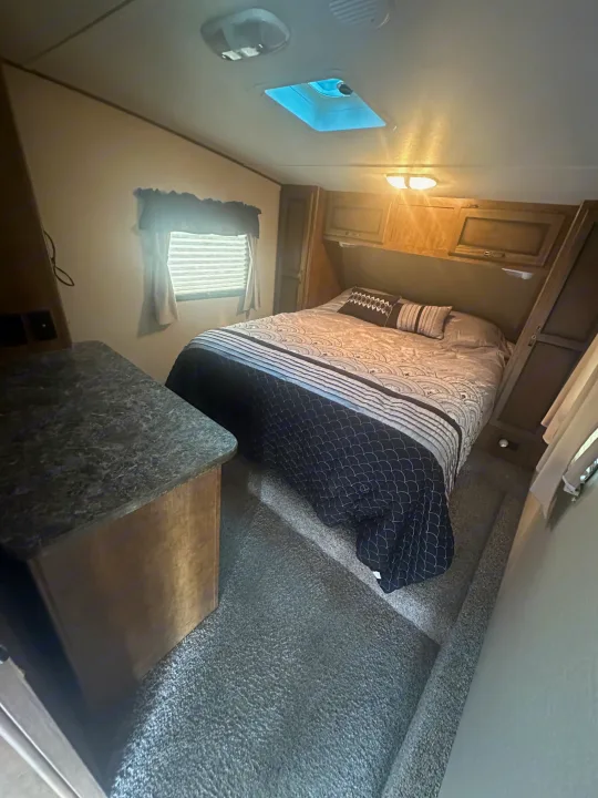 Cozy RV rental bedroom with a comfy bed, patterned bedding, overhead storage, and a window. Perfect for your next adventure.. Crossroads RV Rezerve 2016