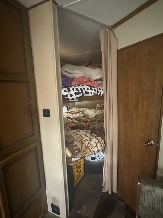 Cozy RV rental interior with two bunk beds, made up with bedding, and a privacy curtain. Includes a wall thermostat and storage space.. Crossroads RV Rezerve 2016