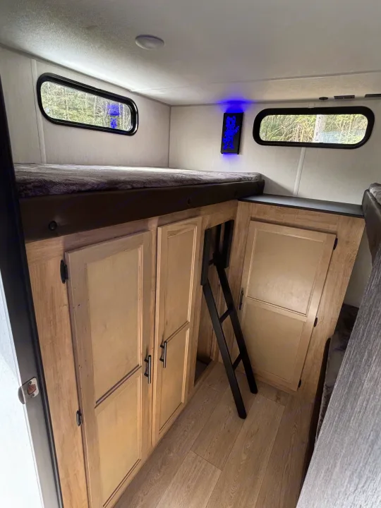Inside an RV rental: a cozy bunk bed area with storage cabinets below and a ladder for access. Forest views from windows.. Forest River Cherokee Grey Wolf 29TE 2026