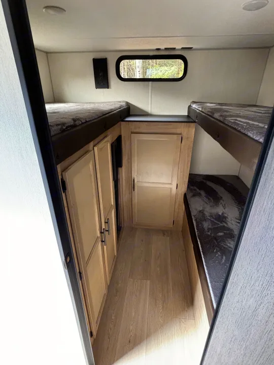 This RV rental bunkhouse interior features light wood-look flooring and cabinets, with comfy twin bunks on both sides, ideal for travel and camping.. Forest River Cherokee Grey Wolf 29TE 2026