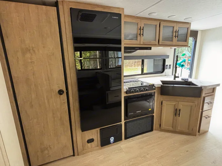 Inside an RV rental: a well-equipped kitchen featuring black appliances, light wood cabinets, and a large sink.. Forest River Cherokee Grey Wolf 29TE 2026