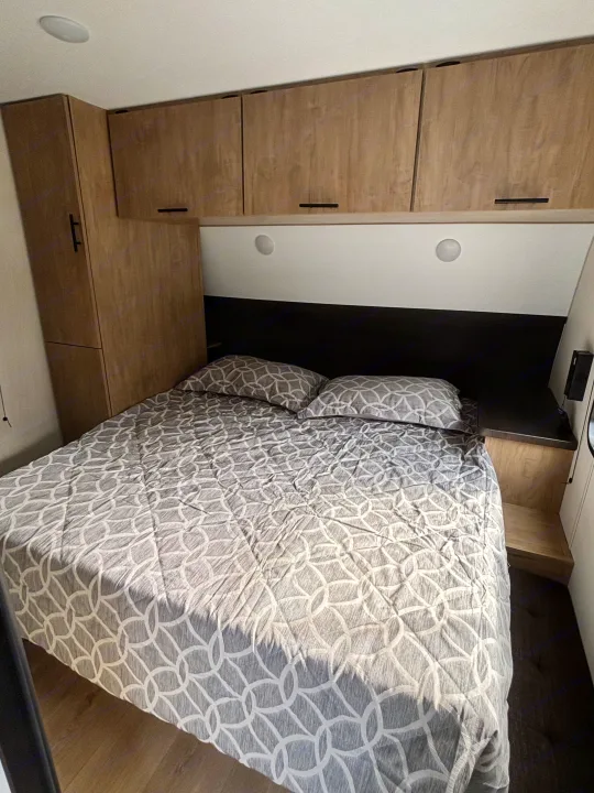 Compact RV rental bedroom featuring a comfy bed with patterned bedding, overhead cabinets, and built-in lighting.. Forest River Cherokee Grey Wolf 29TE 2026