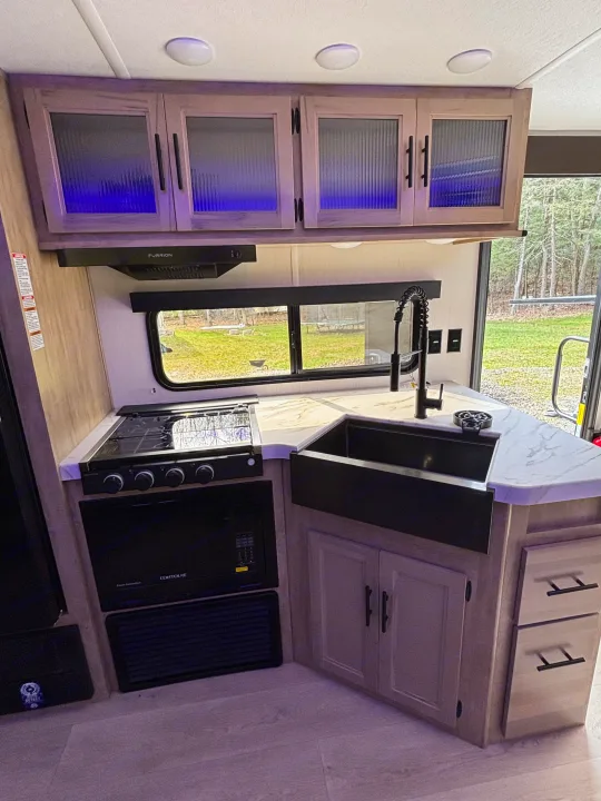 Modern RV rental kitchen featuring blue-lit cabinets, a compact stove, sink, microwave, and outdoor views.. Forest River Cherokee Grey Wolf 29TE 2026