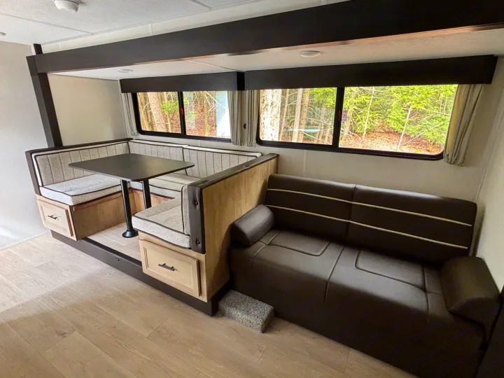 Interior of an RV rental with a light wood dinette, striped cushions, and a dark leather-look sofa.. Forest River Cherokee Grey Wolf 29TE 2026