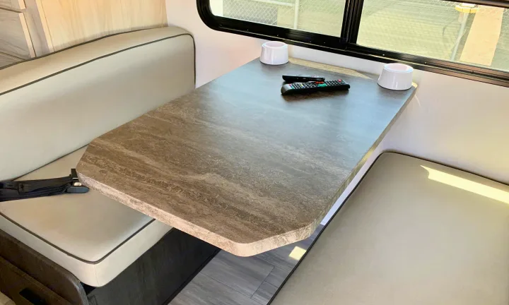 RV rental interior showing a dinette with a gray patterned table, remotes, cup holders, and light-colored seating.. Forest River Sunseeker LE 2023