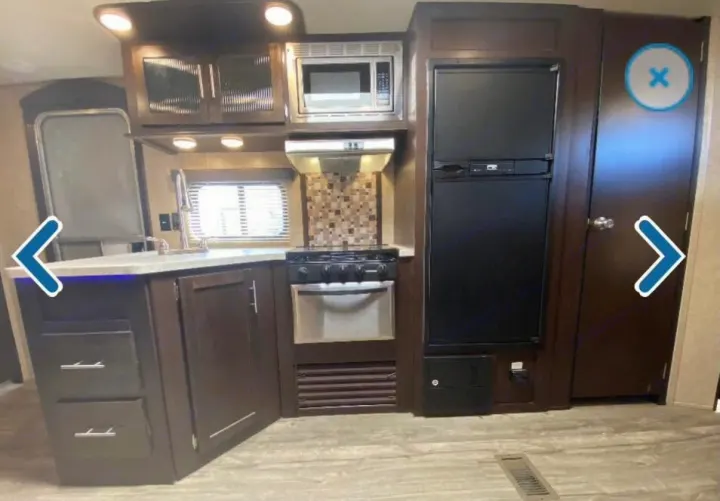 This RV rental kitchen features a sink, microwave, stove, oven, fridge, and ample dark wood cabinets, perfect for on-the-road cooking.. Forest River Cherokee 2018