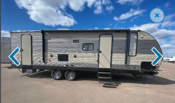 Modern RV rental travel trailer with two doors, pull-out steps, tandem axles, and a rolled awning, parked outdoors.. Forest River Cherokee 2018