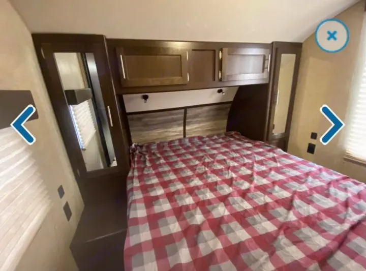 Cozy RV rental bedroom with a red and white checkered bed, overhead cabinets, and mirrored side wardrobes for your comfort.. Forest River Cherokee 2018