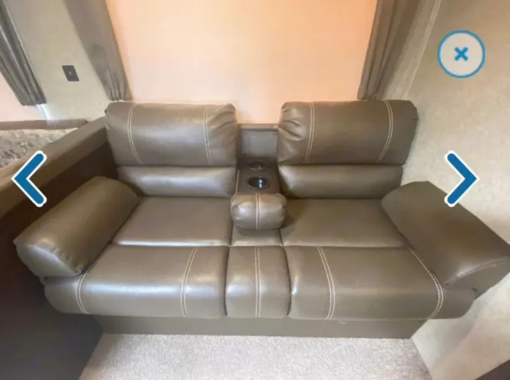 This RV rental features a comfortable brown faux leather two-seater recliner sofa with white stitching & center console cup holders.. Forest River Cherokee 2018