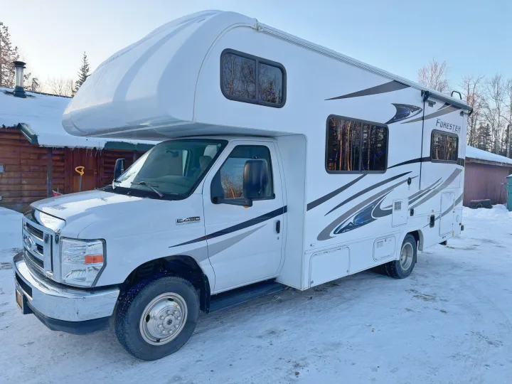 White Class C rv rental parked on snowy ground in front of a rustic cabin, ready for winter adventures.. Forester Forester Motorhome 2020