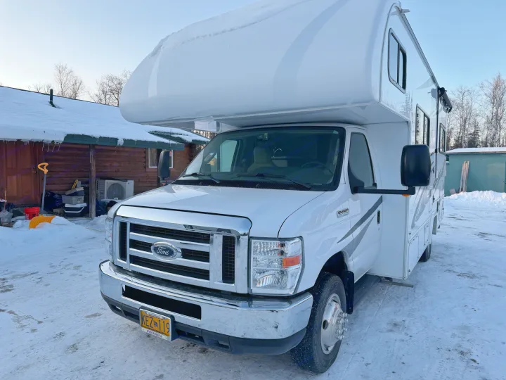 White Class C rv rental, a Ford E-450, covered in snow, parked near a cabin in a winter landscape.. Forester Forester Motorhome 2020