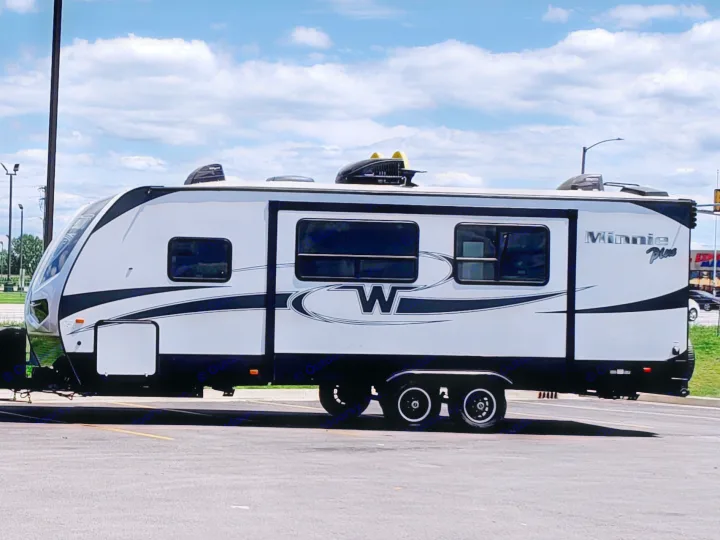 This sleek, white Winnebago Minnie Plus travel trailer, ideal for an rv rental, is parked in a lot under a partly cloudy sky.. Minnie Minnie Plus 2019