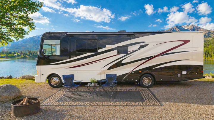 Lakeside RV rental setup with chairs, rug, and fire pit, backed by majestic mountains and a clear blue sky.. Coachmen Pursuit 2014