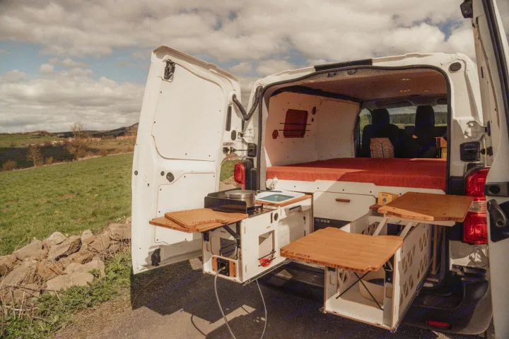 RV rental camper van with open rear doors, showcasing a pull-out mobile kitchen, bed, and outdoor cooking setup in nature.. Renault TRAFIC 2022