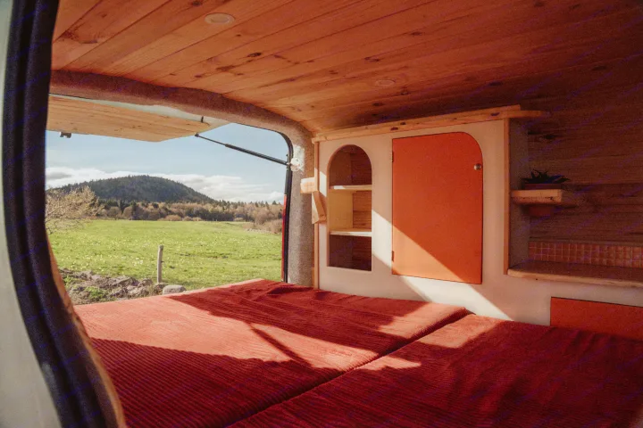 An inviting rv rental interior with a comfy bed and bespoke wooden details, offering expansive nature views from the open camper van.. Renault TRAFIC 2022