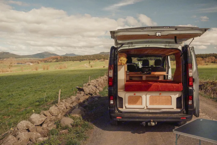 This cozy rv rental, with its back open revealing a custom interior, red bed, and storage, offers scenic mountain views.. Renault TRAFIC 2022