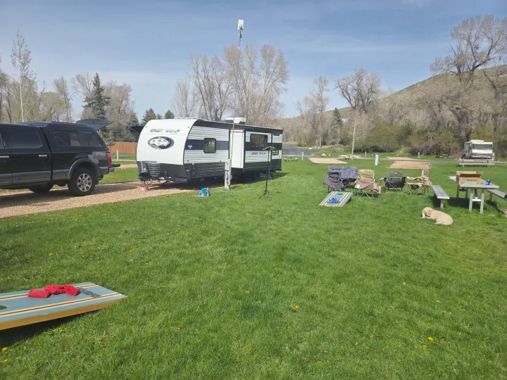 Campsite fun with an RV rental travel trailer, pickup truck, dog, and games. A tall antenna pole hints at connected camping.. Forest River Cherokee Grey Wolf 2024