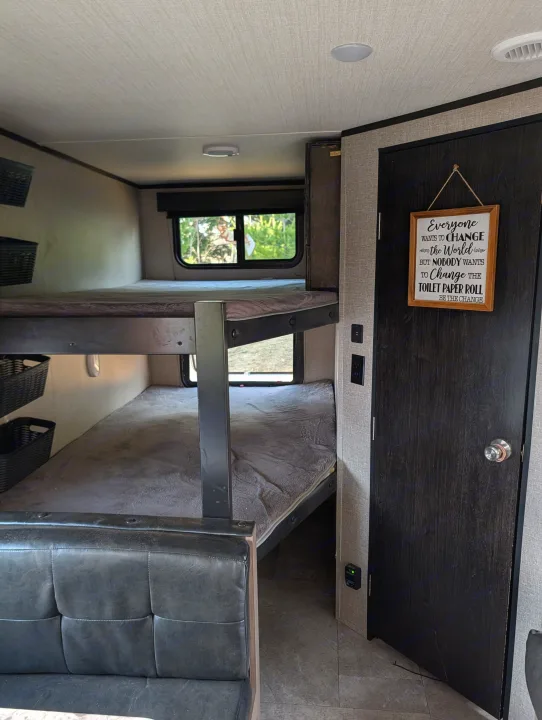 RV rental bunk beds & door with a funny 'change the toilet paper roll' sign, offering a cozy interior.. Grand Design Transcend 2020