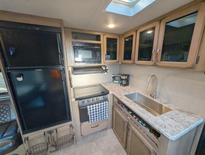 An RV rental kitchen featuring a large fridge, microwave, stove, sink, and small appliances like a coffee maker.. Grand Design Transcend 2020