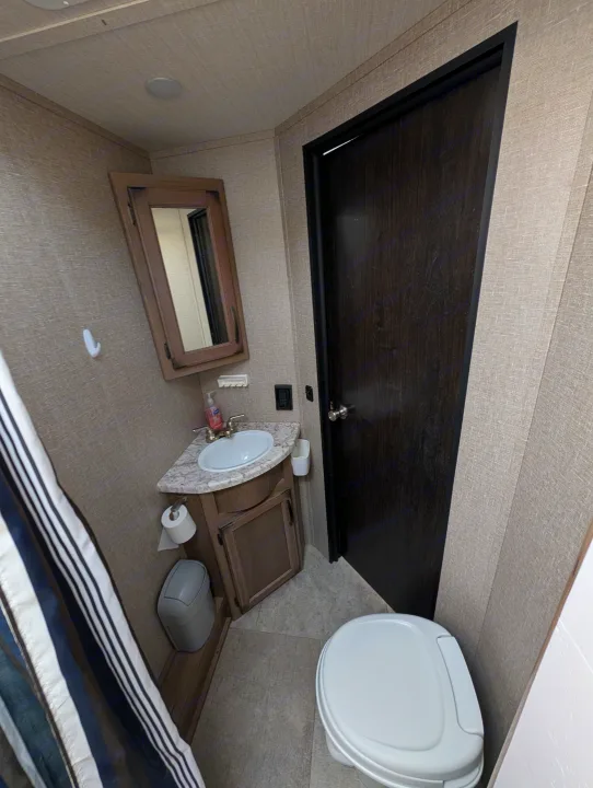 Inside an RV rental, this compact bathroom features a toilet, sink vanity with mirror, and shower area. Efficient use of space.. Grand Design Transcend 2020