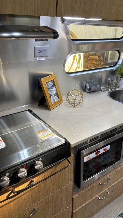 Compact RV rental kitchen featuring a stovetop, microwave, sink, and modern cabinetry with a stainless steel backsplash.. Airstream Flying Cloud 2018