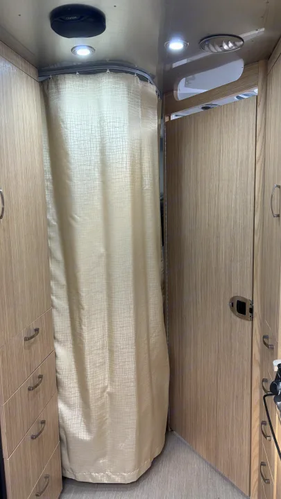 RV rental interior: A beige shower curtain drawn for privacy, flanked by light wood cabinets, with a ceiling speaker and light.. Airstream Flying Cloud 2018