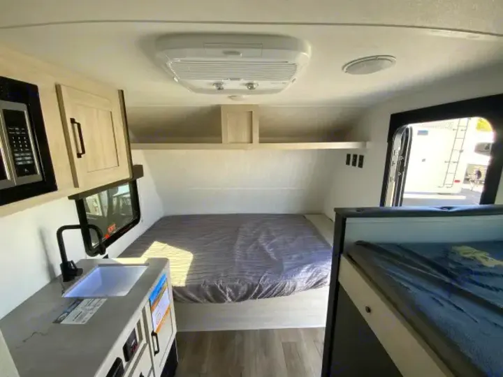 RV rental: Bright interior with a compact kitchen, bed, microwave, and a bunk bed, ready for travel.. Forest River Puma 2025