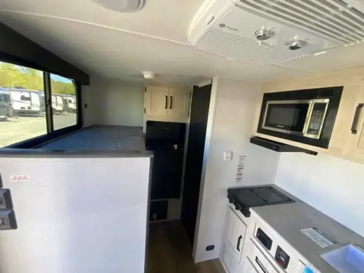 Interior of an RV rental featuring a raised bed/bunk, compact kitchen with microwave, stovetop, and ceiling AC.. Forest River Puma 2025