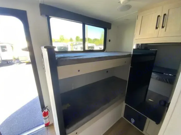View inside an rv rental, featuring bunk beds, a compact kitchen with upper cabinets, and a door with a fire extinguisher.. Forest River Puma 2025