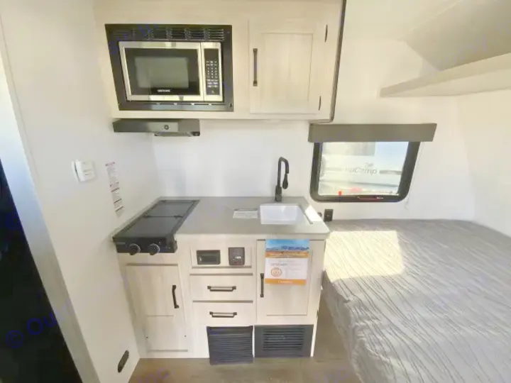 Compact rv rental interior featuring a kitchen with microwave, stove, sink, and cabinetry, adjacent to a cozy bed.. Forest River Puma 2025