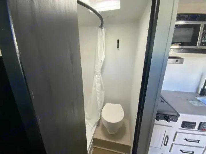Compact RV rental interior: A small wet bath with toilet and shower, adjacent to the kitchen area with a microwave.. Forest River Puma 2025