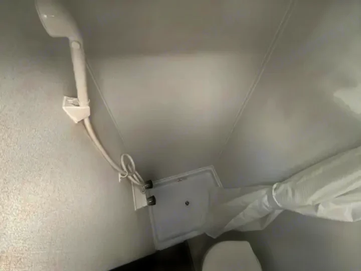 Compact white shower and toilet area inside an RV rental. Features a handheld shower, pan, and a curtain pulled aside.. Forest River Puma 2025