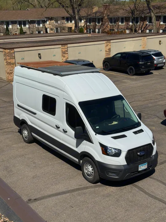White Ford Transit camper van, possibly an rv rental, parked in a lot with solar panels and a roof deck.. Ford Transit 250 AWD 2022