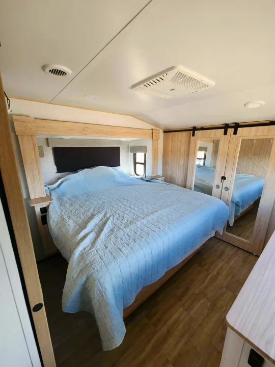 Modern RV rental bedroom featuring a large bed, light wood headboard, and mirrored sliding closet doors.. Alliance RV Avenue 2022
