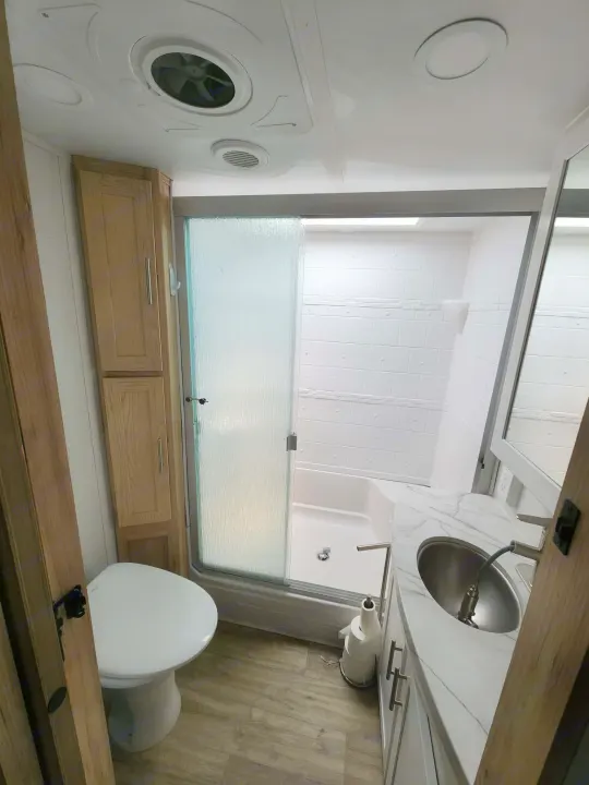 Modern RV rental bathroom with a white toilet, shower with glass door, stainless sink, and wood-look cabinets. Clean and functional.. Alliance RV Avenue 2022