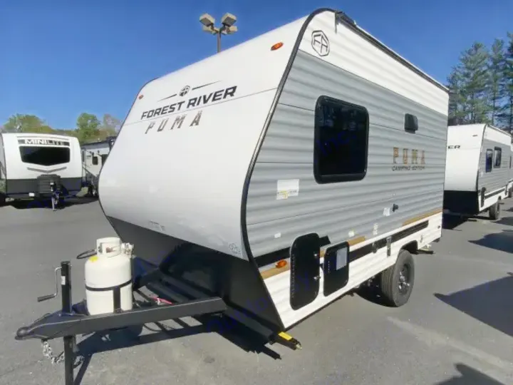 This Forest River Puma travel trailer, a fantastic RV rental option, is shown in white and grey, parked on a lot with a propane tank.. Forest River Puma 2025