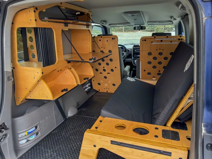 This custom camper conversion shows a modular wooden interior in a small SUV, perfect for an rv rental adventure. Features a bed, storage, and fold-out table.. Honda Element 2010