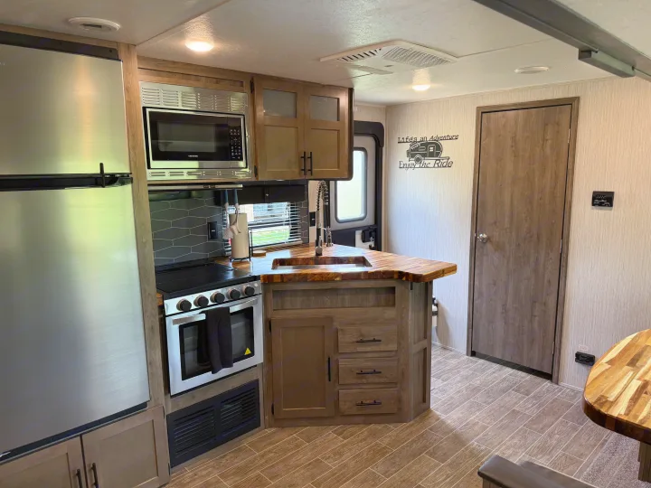 Inside an RV rental: kitchen area with stainless appliances, wood countertops, and "Enjoy the Ride" wall decor.. Forest River Palomino Puma 2021