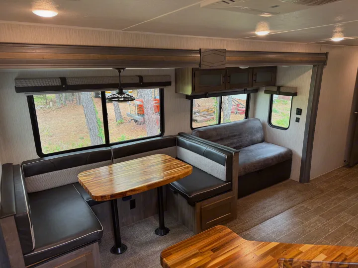 Modern RV rental interior: U-shaped dinette with wood table and a comfy sofa by the window, offering outdoor views.. Forest River Palomino Puma 2021