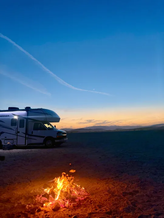 RV rental camping at dusk, with a cozy campfire, distant mountains, a crescent moon, and a bright star in the blue-orange sky.. Forest River Sunseeker 2026